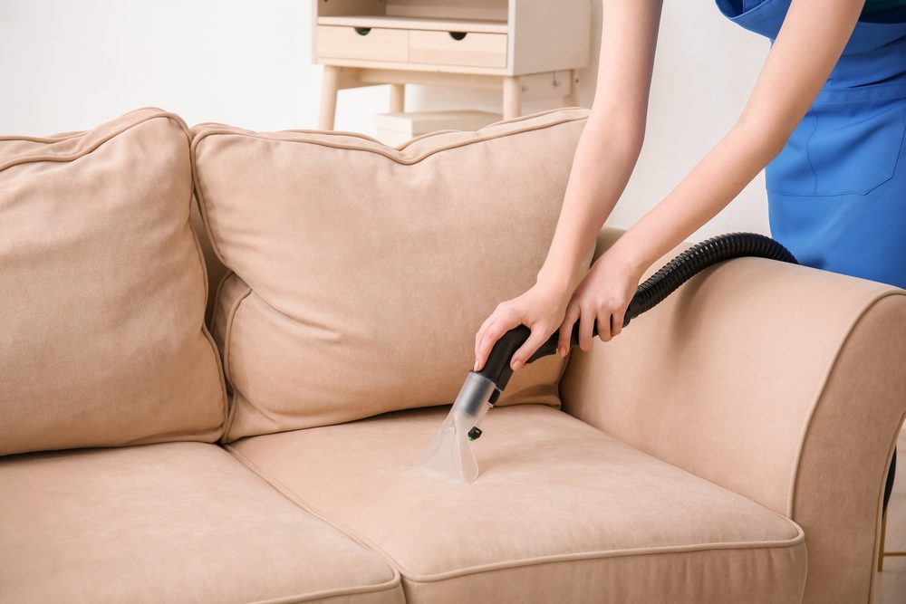 A person using a vacuum on the back of a couch.